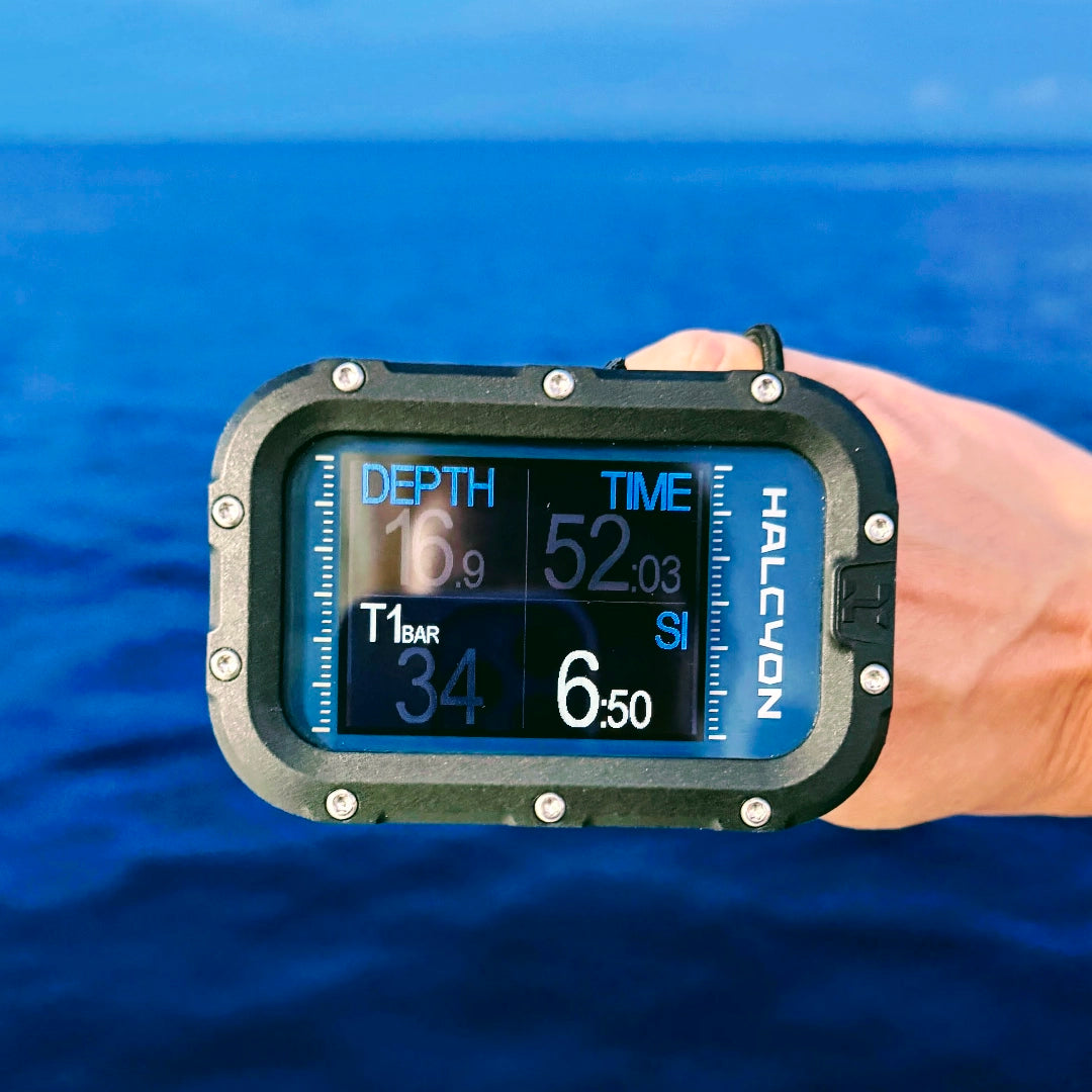 Halcyon Symbios Blue Dive Computer in hand with blurred sea in the background