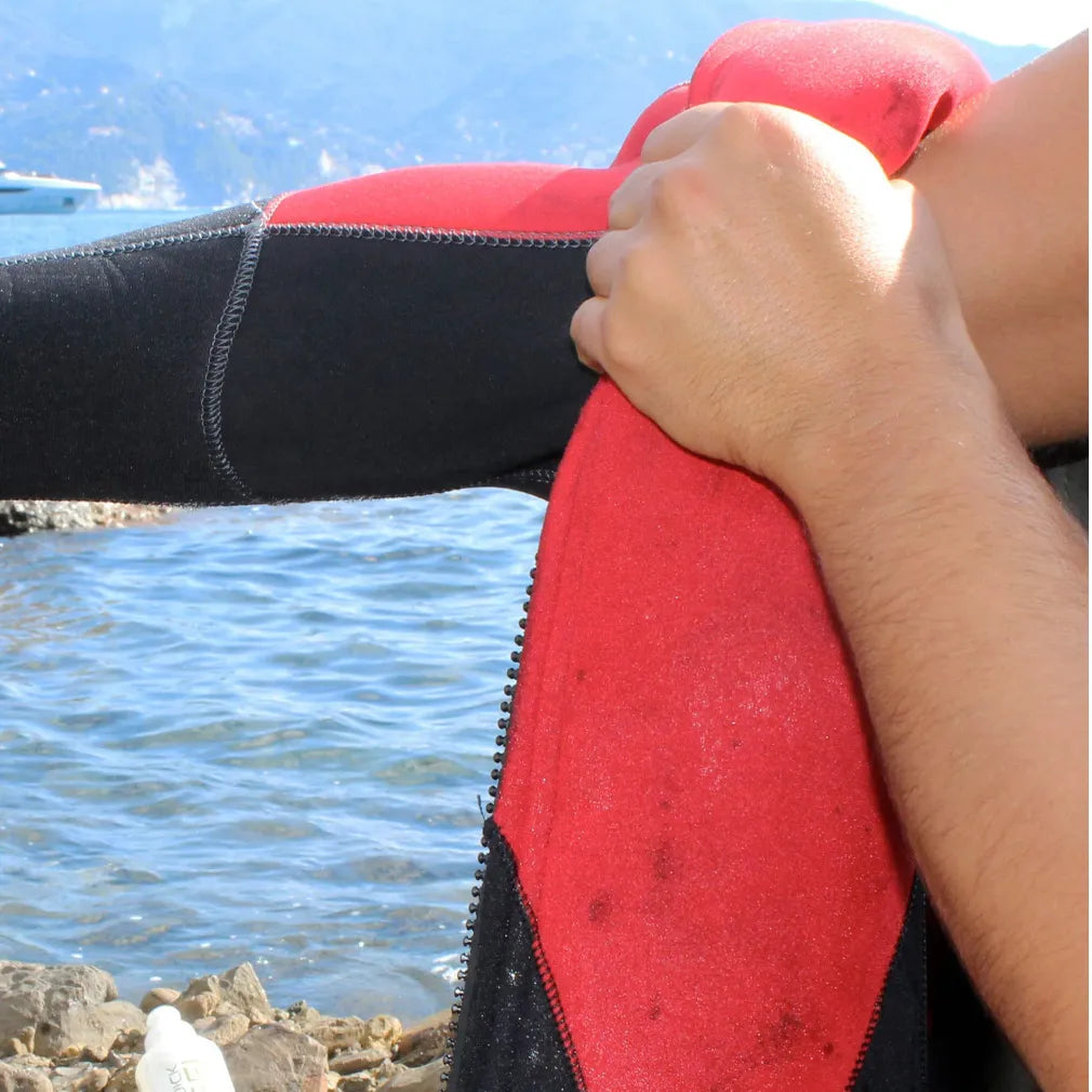 Person holding a red and black wetsuit by the water