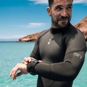 Scuba divers in a Fourth Element Xenos ARC Wetsuit checking his watch with a scenic ocean background