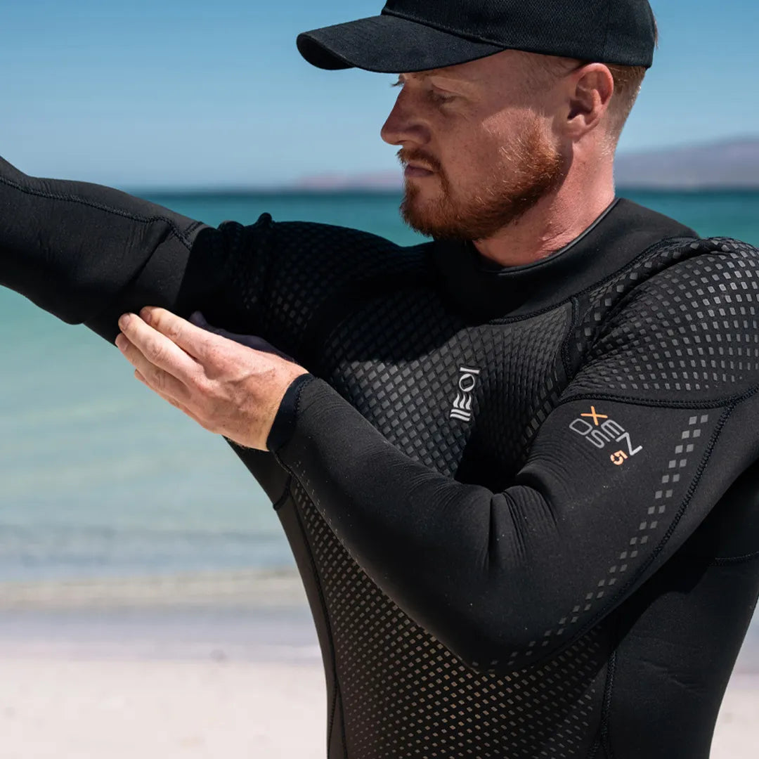 Man wearing a black Fourth Element Xenos ARC Wetsuit on a beach