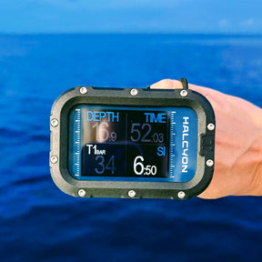 Halcyon Symbios Blue Dive Computer in hand with blurred sea in the background