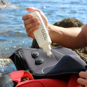 Person applying Look Clear Quick Gel to a wetsuit by a body of water
